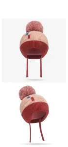 Detail of pink and brown winter knit hat with earflaps and fluffy pom pom for kids