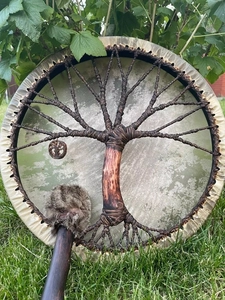 Detail view of Shaman drum with tree of life woven pattern and fur mallet on grass