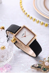 Detail of square gold watch with white dial on crown stand and luxury accessories