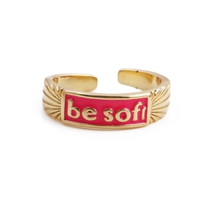 Detail of adjustable gold ring featuring pink enamel with 'be soft' text and textured band