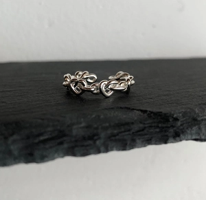 Close-up of silver heart chain ring on dark rock surface showing metallic texture
