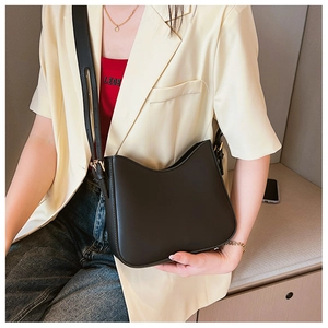 Close-up of black leather shoulder bag with gold hardware and adjustable strap on a model