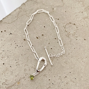 Detailed shot of a silver paperclip chain bracelet with a green gemstone and toggle clasp