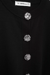 Close-up of black knit cardigan featuring elegant silver spiral textured metal buttons