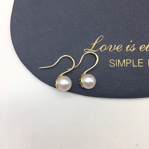 Detail of high-luster freshwater pearl earrings with golden hooks on black leather texture