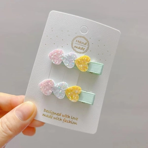 Detail of glitter heart hair clips in pink white yellow on green ribbon wrapped base