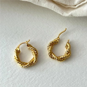 Detailed view of golden twisted hoop earrings on white texture background with linen fabric