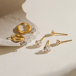 Détail de boucles d'oreilles dorées et clous avec cristaux de zircone ronds sertis griffes