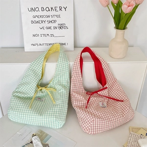 Detail view of plaid canvas tote bags in soft green and red against a minimalist background