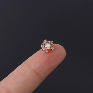 Macro shot of tiny rose gold stud earring with rainbow zircon on a fingertip for size
