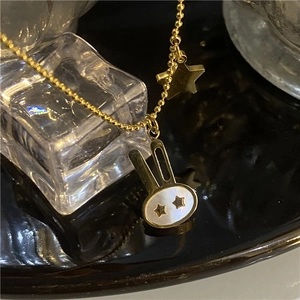 Detail view of a gold beaded chain necklace with a mother-of-pearl bunny and star pendant