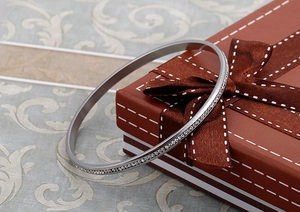 Bracciale rigido in acciaio argento con cristalli pavé esposto su una scatola regalo marrone
