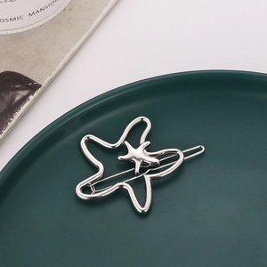 Close-up of a silver starfish hair clip on a green plate with a magazine background