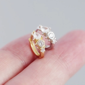 Macro detail of S925 silver huggie earrings with pear-shaped cubic zirconia on fingertips
