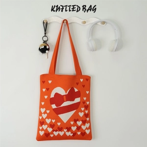 Detail of orange knitted tote bag with large red heart and bow on wavy wall hook