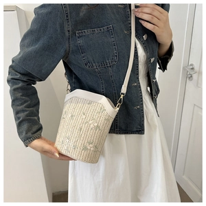 Détail du sac seau en paille tissée avec broderie florale et bandoulière sur un modèle