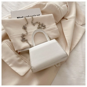 Detail view of a white mini trapezoid bag with silver chain strap on beige fabric