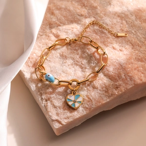 Golden elephant heart bracelet with blue enamel eye charm on pink mineral stone background