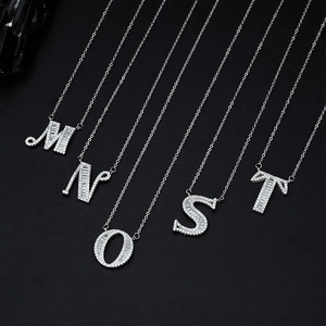 Silver letter pendants M, N, O, S, T with zircon stones on thin O-chains over black background