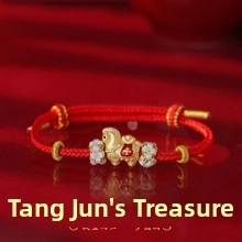 Detailed shot of golden horse charm with red enamel on a woven lucky rope bracelet