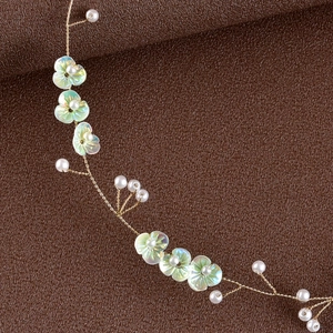Macro detail of handmade bridal headband with iridescent green flowers and faux pearls