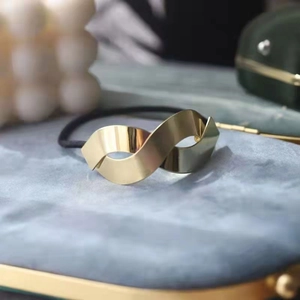 Elegant gold metal ribbon twist hair tie with black elastic band on marble base
