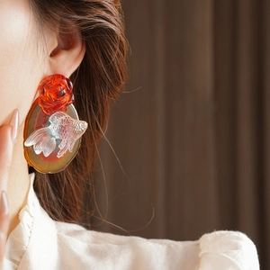 Close-up of artistic floral earring with red rose and transparent fish on amber base