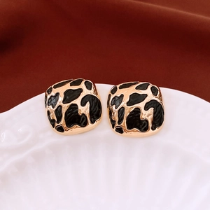 Macro detail of square gold earrings with black leopard enamel on white ceramic dish