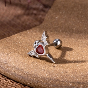 Macro view of gothic bat wing cartilage stud with red heart zircon on dark stone
