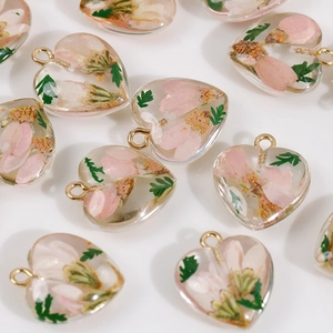 Macro shot of heart-shaped resin pendants with pink dried flowers and golden loops