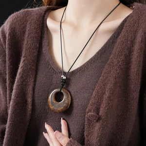 Detail view of a brown stone pendant necklace worn by a model on a black cord