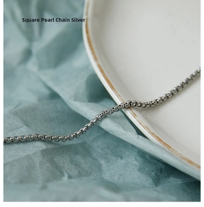 Detailed close-up of a silver box chain link necklace on a minimalist blue backdrop