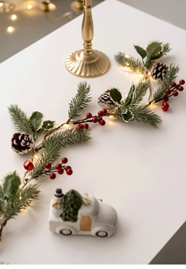 Macro detail of LED Christmas garland with pine cones, red berries and warm lights