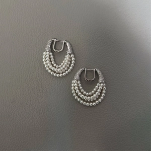 Detail view of triple-row pearl tassel earrings with silver horseshoe buckle and texture