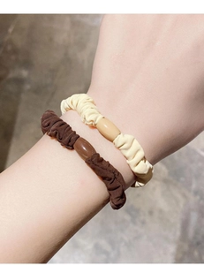 Close-up of beige and dark brown elastic scrunchies with bead accents on a wrist