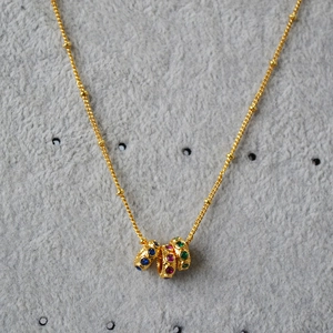 Détail d'un collier doré avec pendentif en zircon coloré sur fond gris texturé