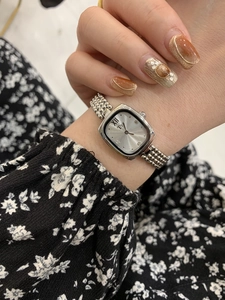 Detail of silver square dial women's watch with steel bracelet on wrist with floral background