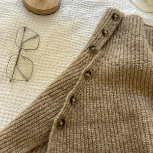 Macro detail of knit sweater featuring brown buttons and chunky knit texture in khaki