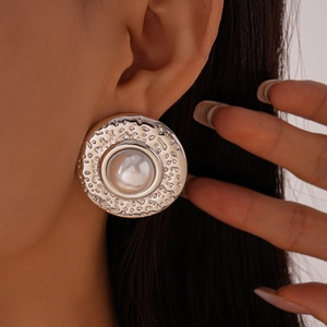 Close-up of silver hammered metal earrings with central white bead on a model