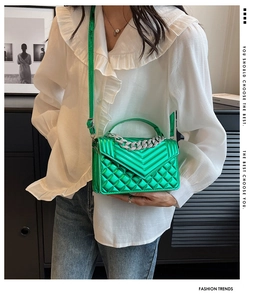 Détail d'un sac à main vert émeraude matelassé avec une poignée en chaîne argentée chic
