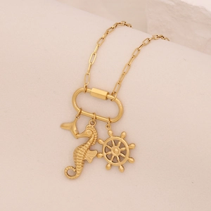 Detail of gold necklace featuring seahorse, ship wheel and anchor charms with oval links