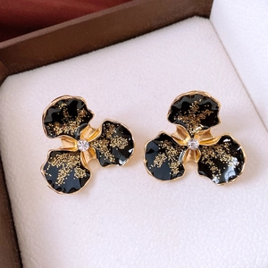 Gros plan de boucles d'oreilles fleur en émail noir avec paillettes dorées et cristaux
