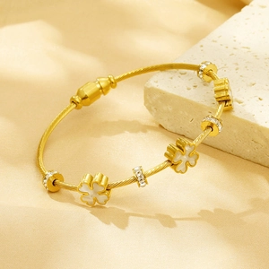 Detail of golden steel wire bracelet with clover charms and shimmering rhinestones