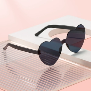 Fashionable heart-shaped rimless sunglasses with dark lenses on a pink background