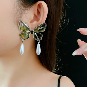 Macro view of green butterfly earrings with glitter wings and hanging pearl drop pendants