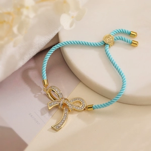 Detailed shot of gold bow charm bracelet with blue cord and sparkling white zircons