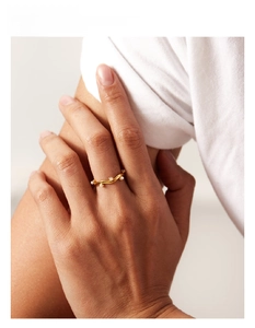 Close-up of a gold wavy band ring with small white pearls on a model's finger