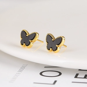 Macro detail of elegant butterfly stud earrings in black and gold on a white ceramic plate