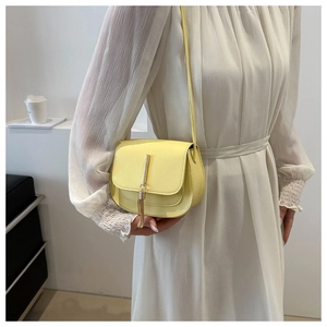 Detail of bright yellow saddle bag with metallic tassel on a minimalist white backdrop