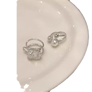 Silver rings featuring a hammer-textured square and large pearl on a white ceramic plate